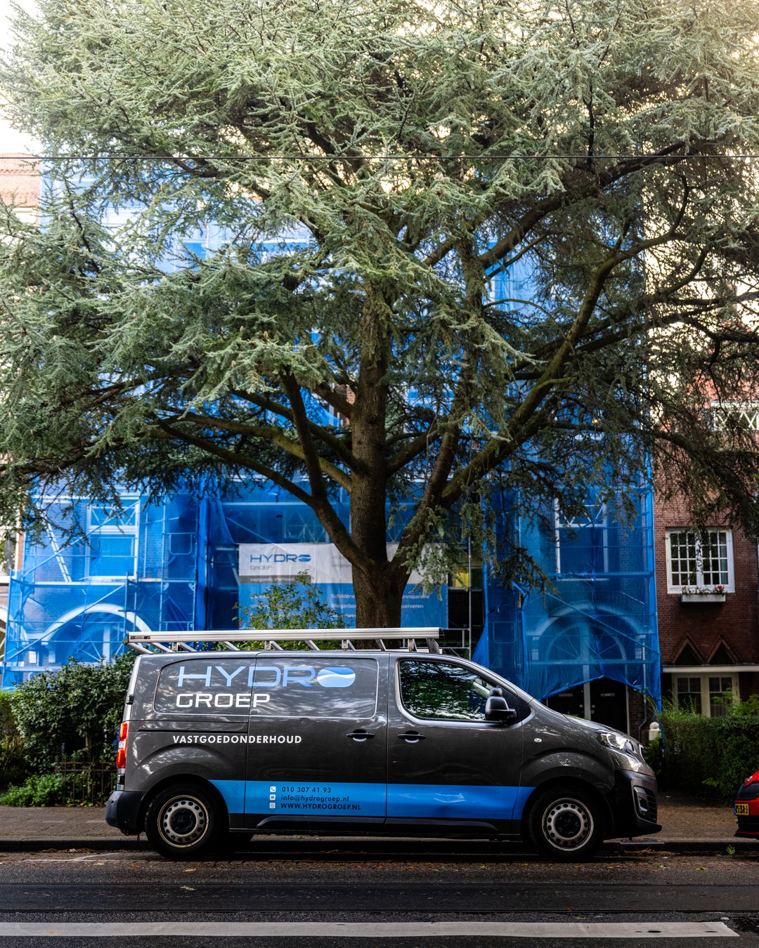 Hydro Groep bedrijfsbus voor steiger aan voorgevel tijdens betonreparatie in Rotterdam