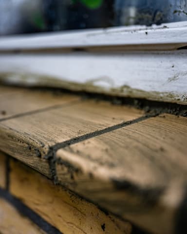Vakman hakt voegwerk uit bij donker metselwerk op steiger in Ridderkerk