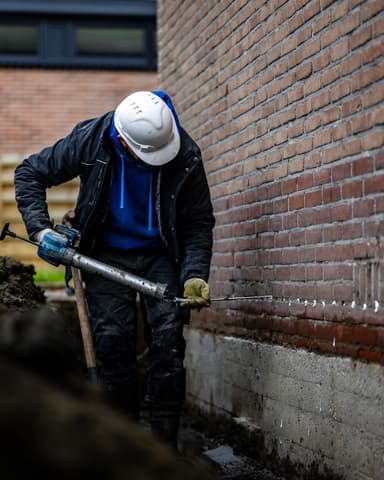 Vakman injecteert buitenzijde gevel vanuit uitgegraven sleuf in Brielle