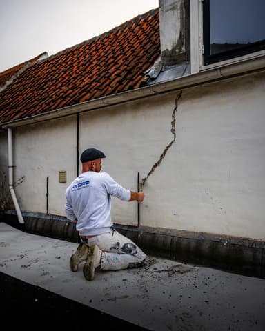 Vakman hakt voegwerk uit op steiger tijdens gevelrenovatie in Brielle door Hydro Groep