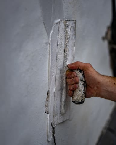 Detail van stucwerk gladstrijken met spaan tijdens gevelrenovatie in Brielle door Hydro Groep