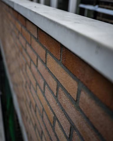 Vakman trekt halfsteens buitenmuur op met waterpas bij betonreparatie in Rotterdam door Hydro Groep