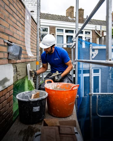 Vakman mengt mortel op steiger bij achtergevel tijdens betonreparatie in Rotterdam door Hydro Groep