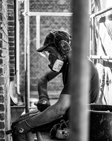 Hydro Groep vakman met stofmasker pauzeert op steiger bij conserveren metselwerk in Rotterdam