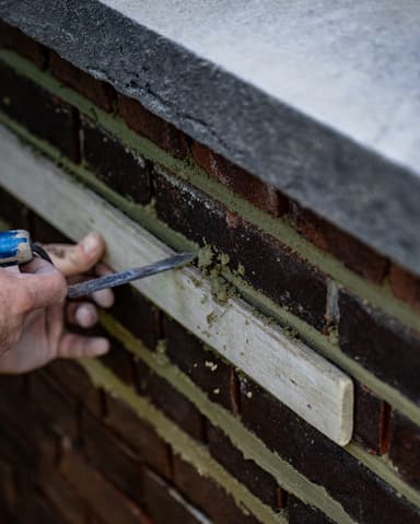 Vakman voegt gevel op steiger met voegspijker tijdens conserveren metselwerk in Rotterdam