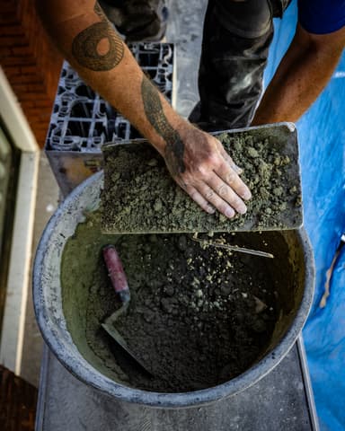 Vakman smeert voegen in met kwast op steiger tijdens conserveren metselwerk in Rotterdam