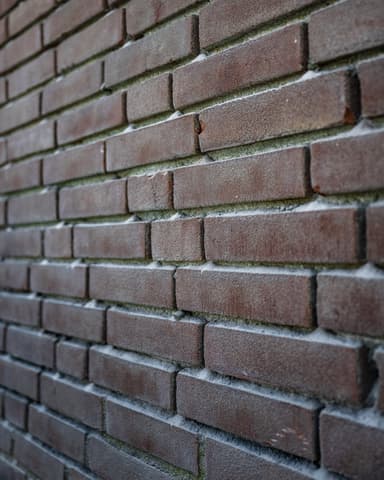 Medewerker met gehoorbescherming hakt voegen uit op zijgevel tijdens conserveren metselwerk Sommelsdijk
