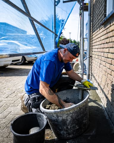 Medewerker brengt nieuw voegwerk aan op gevel naast raam tijdens conserveren metselwerk Dordrecht