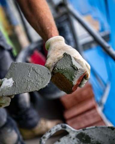 Medewerker schept voegspecie uit kuip op steiger tijdens betonreparatie aan gevel in Den Haag