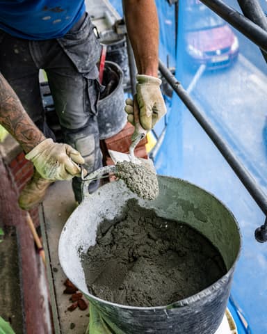 Close-up hand met steen en specie klaar voor inmetselen bij betonreparatie latei in Den Haag