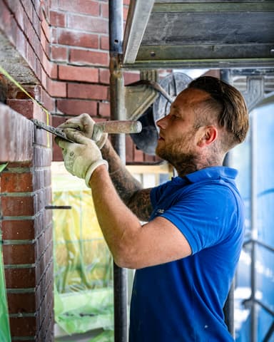 Medewerker metselt nieuwe stenen in boven raamkozijn tijdens betonreparatie aan latei Den Haag