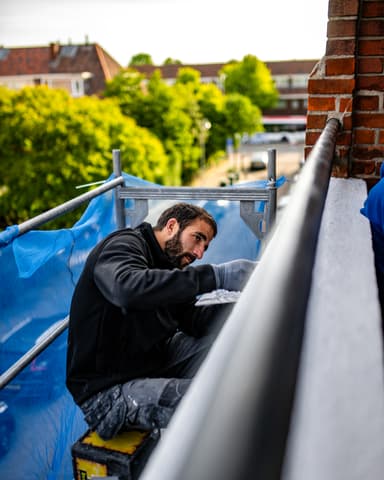 Medewerker repareert voegwerk naast raamkozijn op steiger tijdens betonreparatie VvE Den Haag