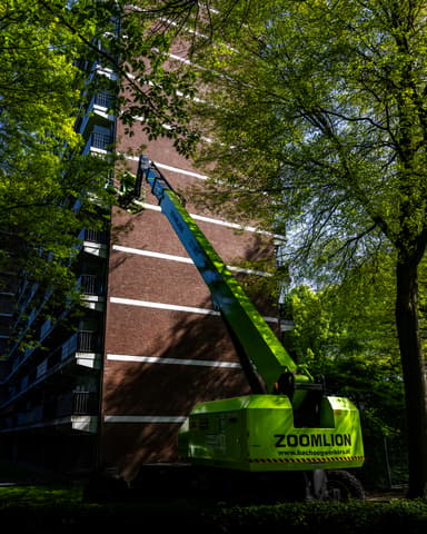 Silhouet van hoogwerker tegen lucht bij kopgevel Meulemansflat tijdens betonreparatie Tilburg