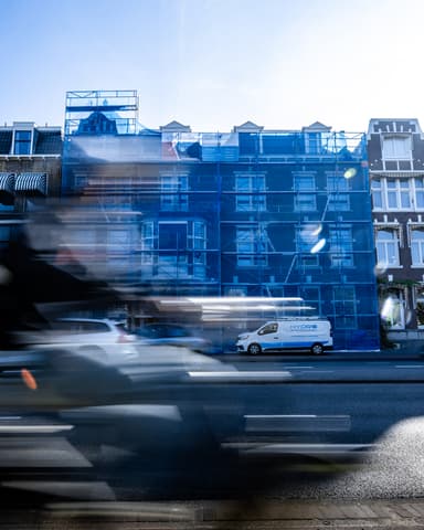 Straatbeeld Raamweg met blauw steigergaas en stadsgezicht tijdens betonreparatie in Den Haag