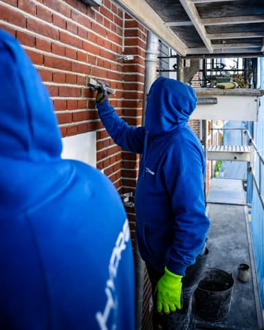 Twee medewerkers voegen gevel op vanaf steiger bij conserveren metselwerk Hofsingel in Vlaardingen