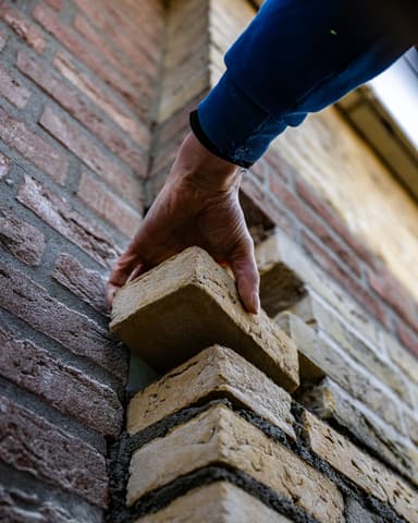 Hand plaatst nieuwe steen bij gevelhoek in Capelle aan den IJssel door Hydro Groep