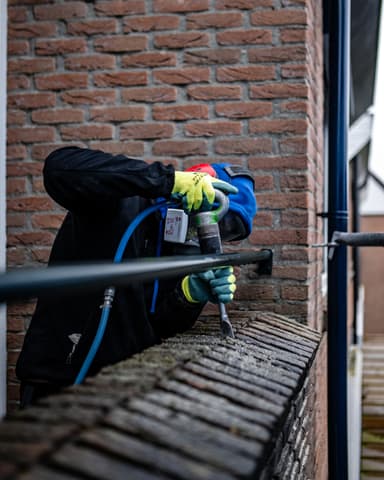 Vakman straalt voegwerk op steiger bij gevel in Rhoon tijdens conserveren metselwerk door Hydro Groep
