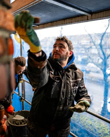 Vakman op steiger achter beschermdoek in Voorburg tijdens betonreparatie door Hydro Groep