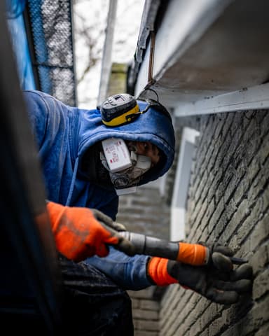Vakman straalt gevel met volledige beschermkleding in Bergschenhoek door Hydro Groep