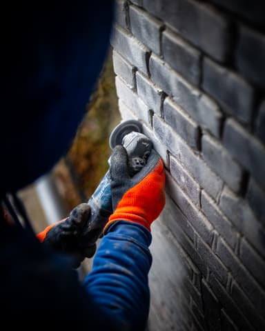 Vakman werkt geknield aan gevel op steiger in Hellevoetsluis tijdens conserveren metselwerk