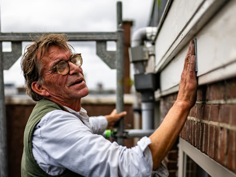 Schilder bewerkt kozijn vanaf steiger tijdens buitenschilderwerk aan woning in Rotterdam