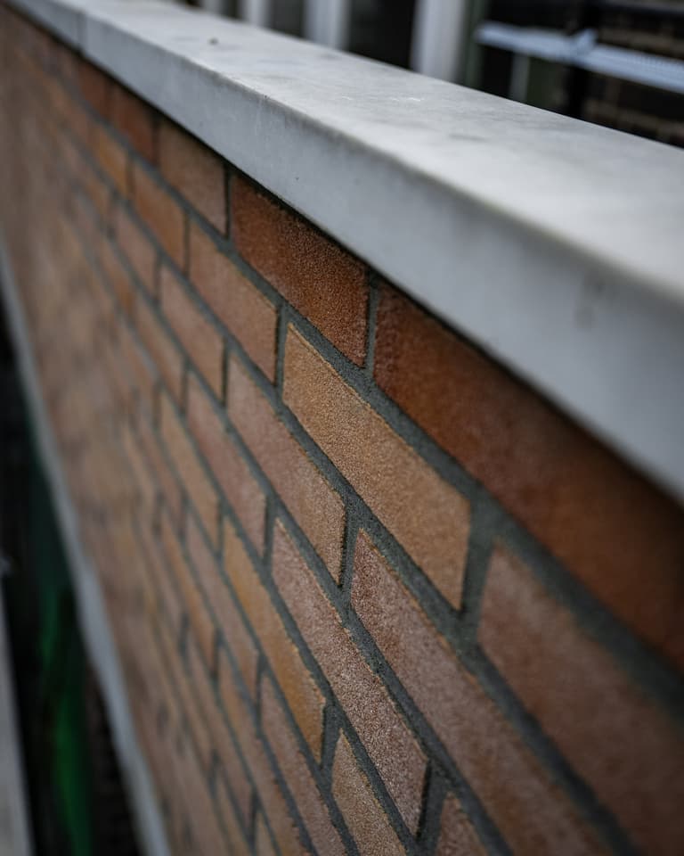 Vakman trekt halfsteens buitenmuur op met waterpas bij betonreparatie in Rotterdam door Hydro Groep